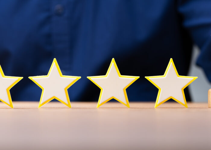 Five wooden stars lined up on a table next to a bell, which is being rung by a hotel worker in white gloves